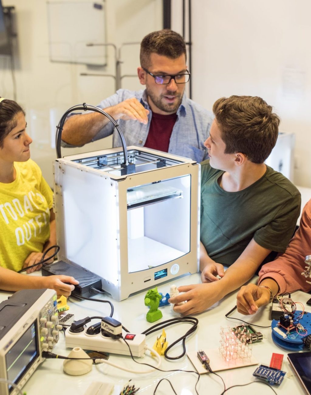 Teens love new technology Group of students, working on some robot project at electronic course, they working with 3D printer on robo arm. Working table full of different oscilloscopes and equpment needed for recording electrical circuits, 3D printer there too.Instructor helping children with project